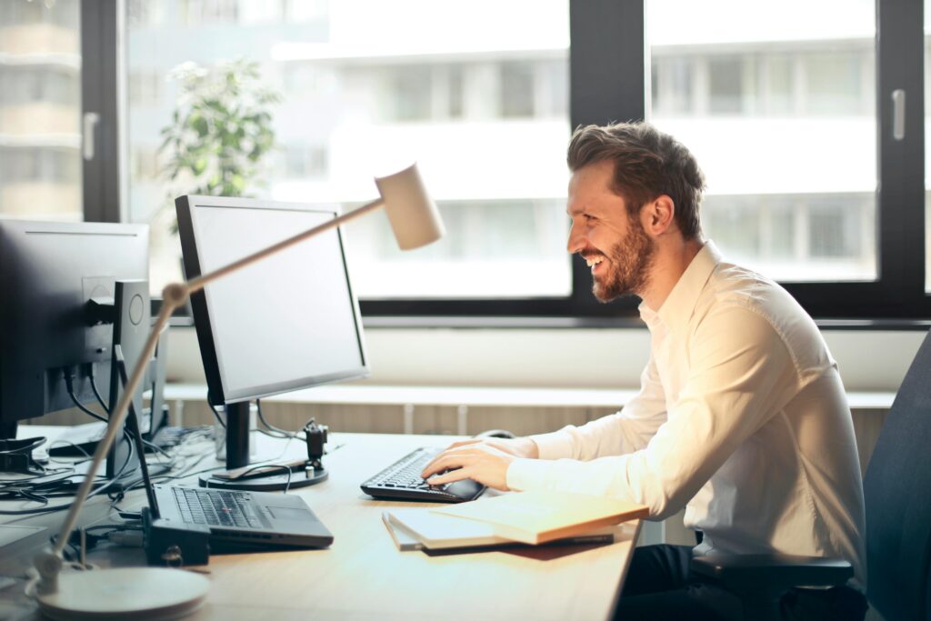 A man sitting in front of a computer smiling because of a promotion.