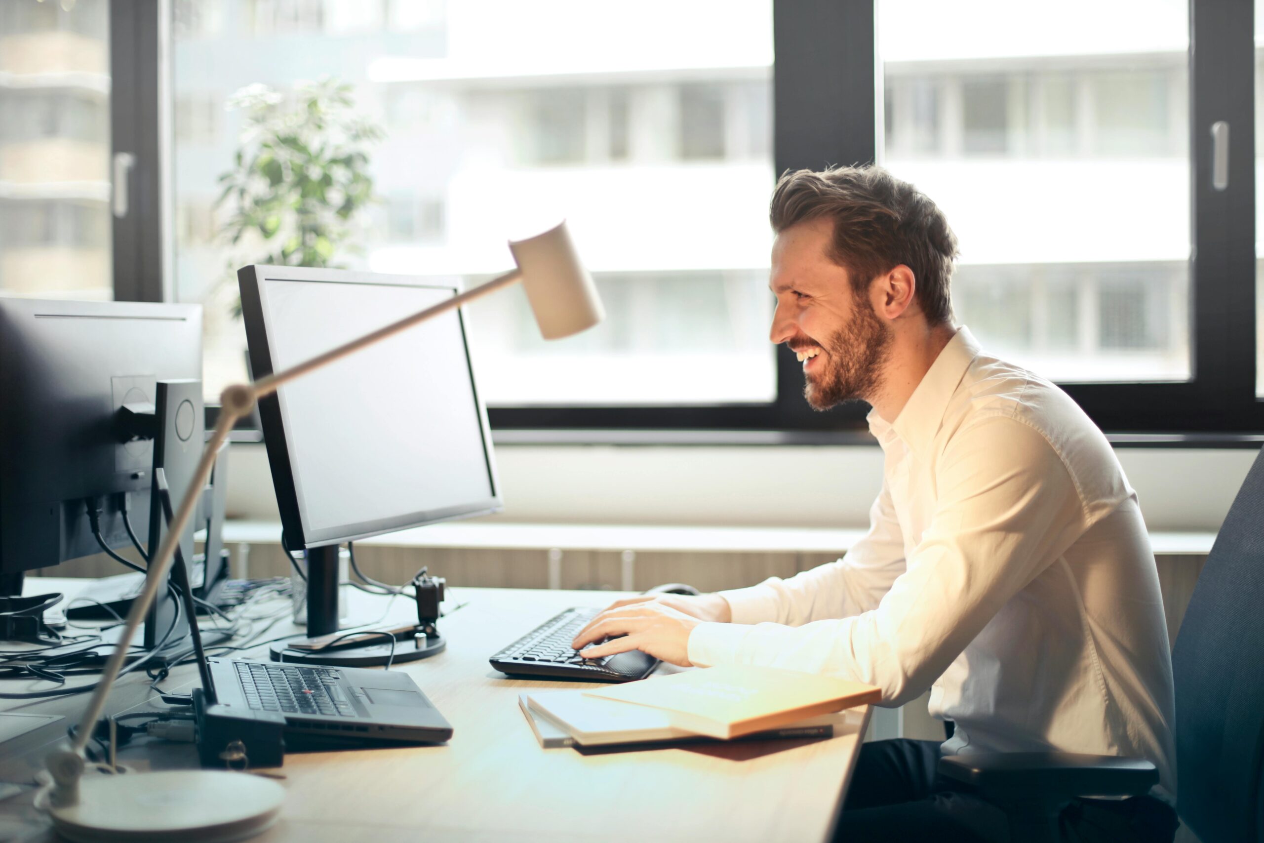 A man sitting in front of a computer smiling because of a promotion.
